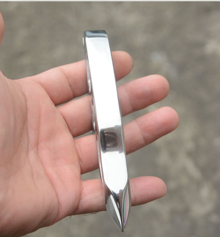 Upright side profile of the mirror-polished steel knuckle duster standing on an open palm with the pointed tip down