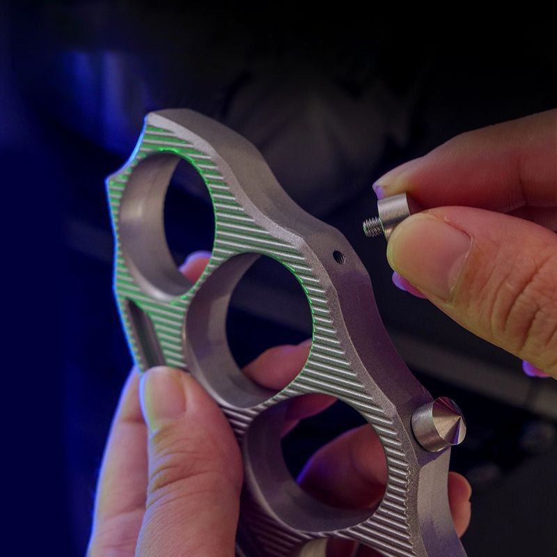 Hands unscrewing the detachable window-breaking cone from the knuckle duster body