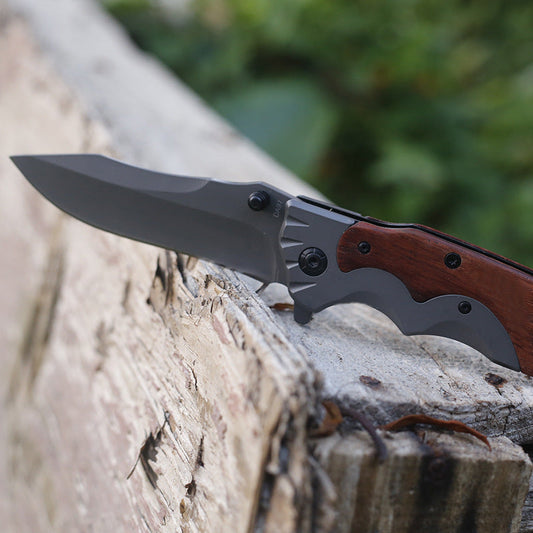 Wood-handle folding knife open beside a closed G10-handle version on a weathered plank