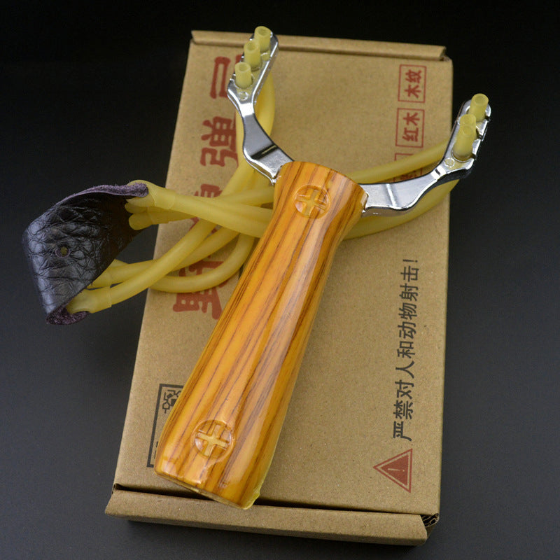 Wood grain slingshot resting on its printed cardboard box showing the leather pouch and yellow band strands