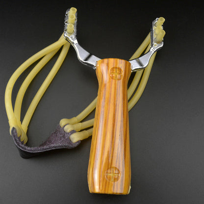 Wood grain water transfer slingshot with yellow band strands and dark leather pouch standing on a dark grey background