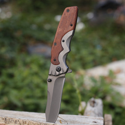 Wood-handle folding knife standing upright on its blade tip, gray bolster and wood scales in view