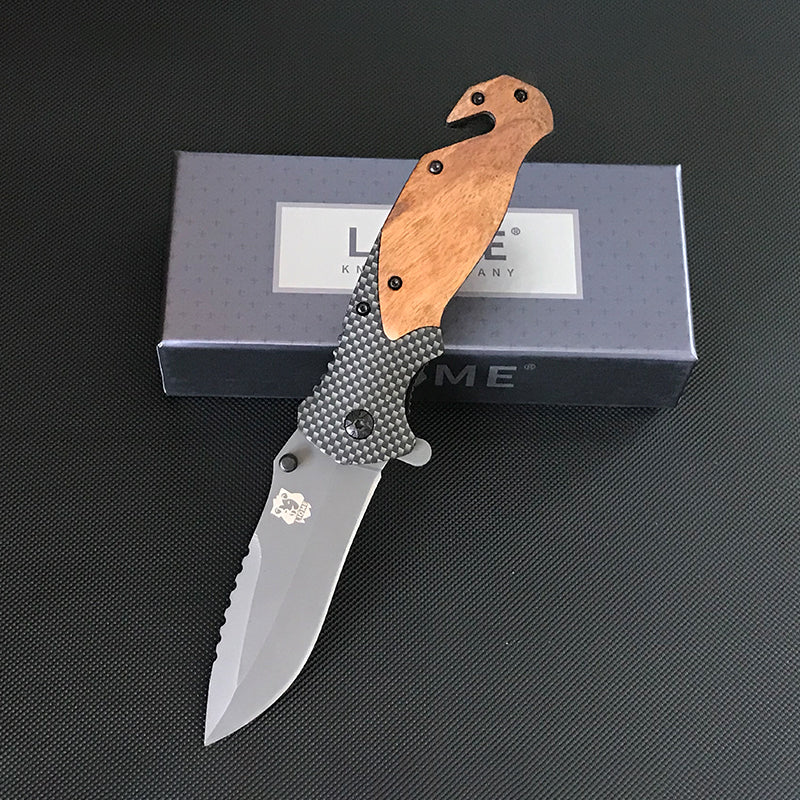 Open Liome X50 folding knife with wooden handle and sawback blade leaning against a Liome Knife Company box