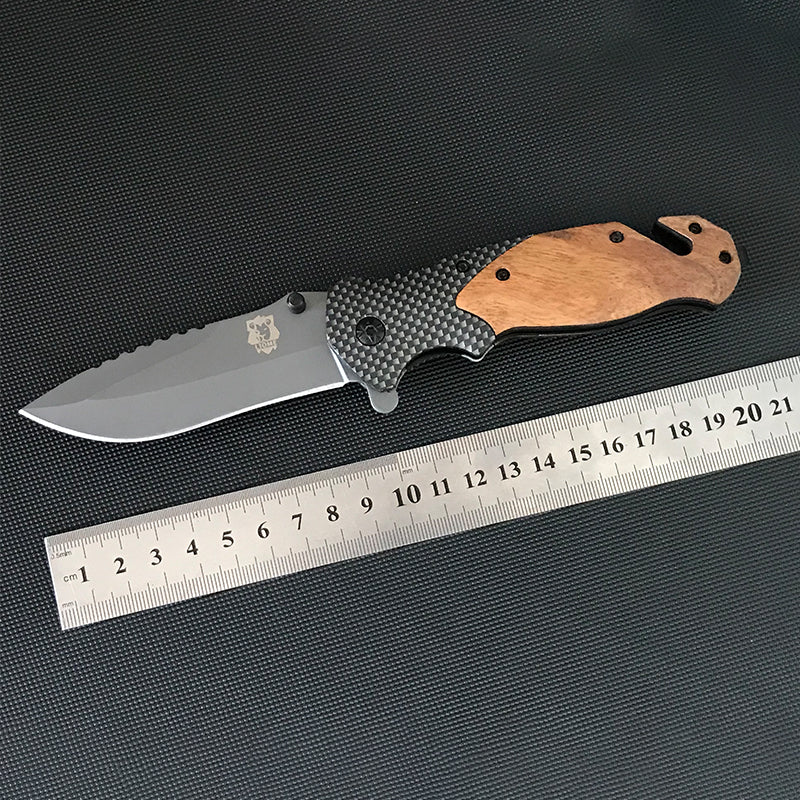 Open Liome X50 folding knife laid above a steel ruler showing about 21cm total length, sawback spine and etched blade crest