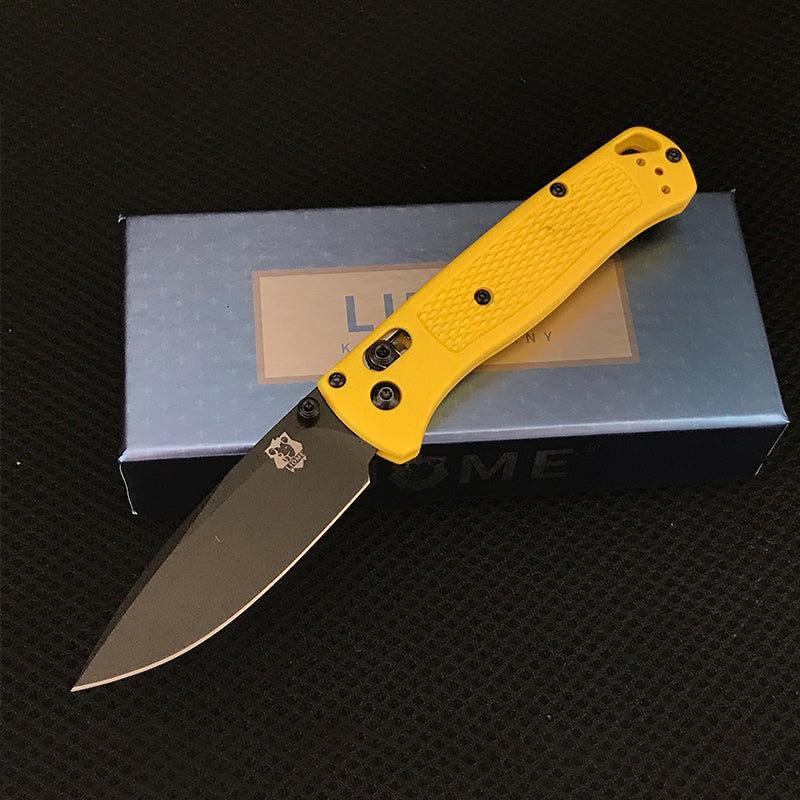 Yellow handled folding knife with black-coated drop-point blade open across a Liome branded box