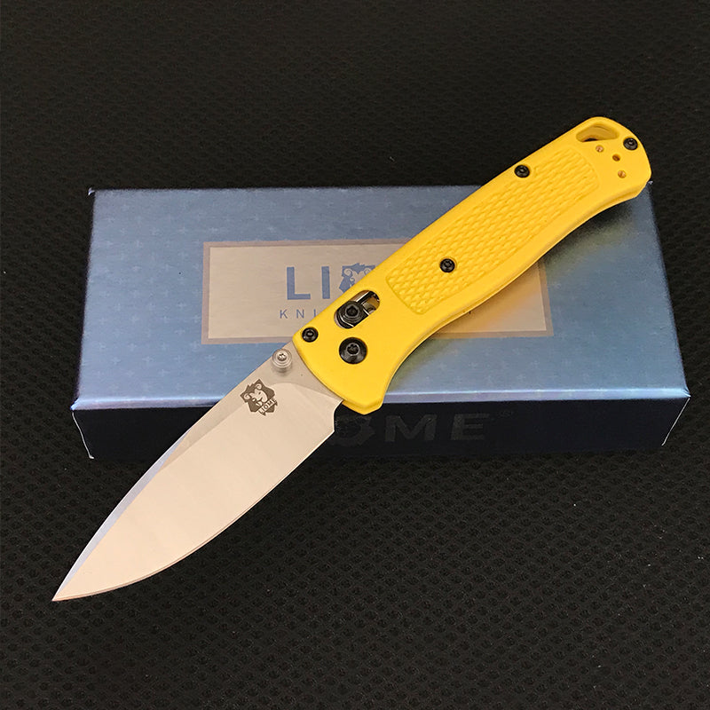 Yellow handled folding knife with polished silver drop-point blade open on a Liome branded box